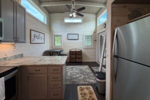 Tiny house kitchen on Highland Hill Lane with stainless appliances, light wood walls, and a dining nook by two windows.