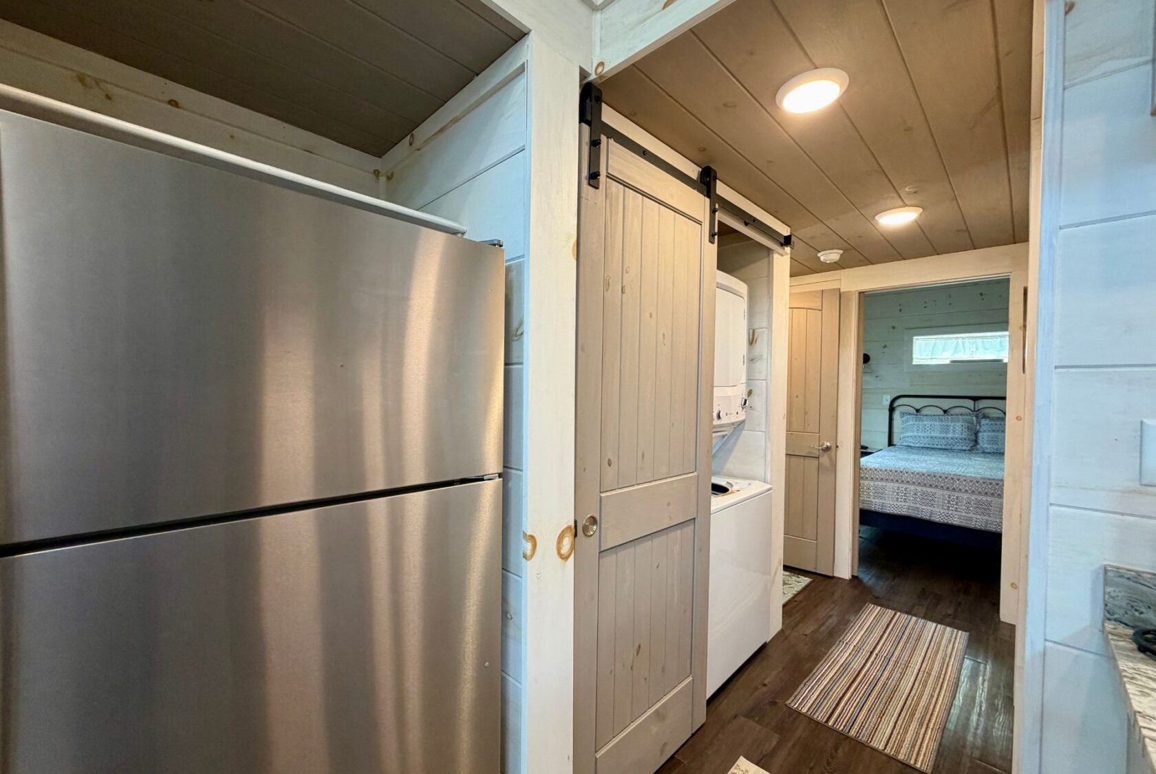 A stainless steel fridge by the laundry closet; washer, dryer, and a bedroom visible in 23 Highland Hill’s open layout.
