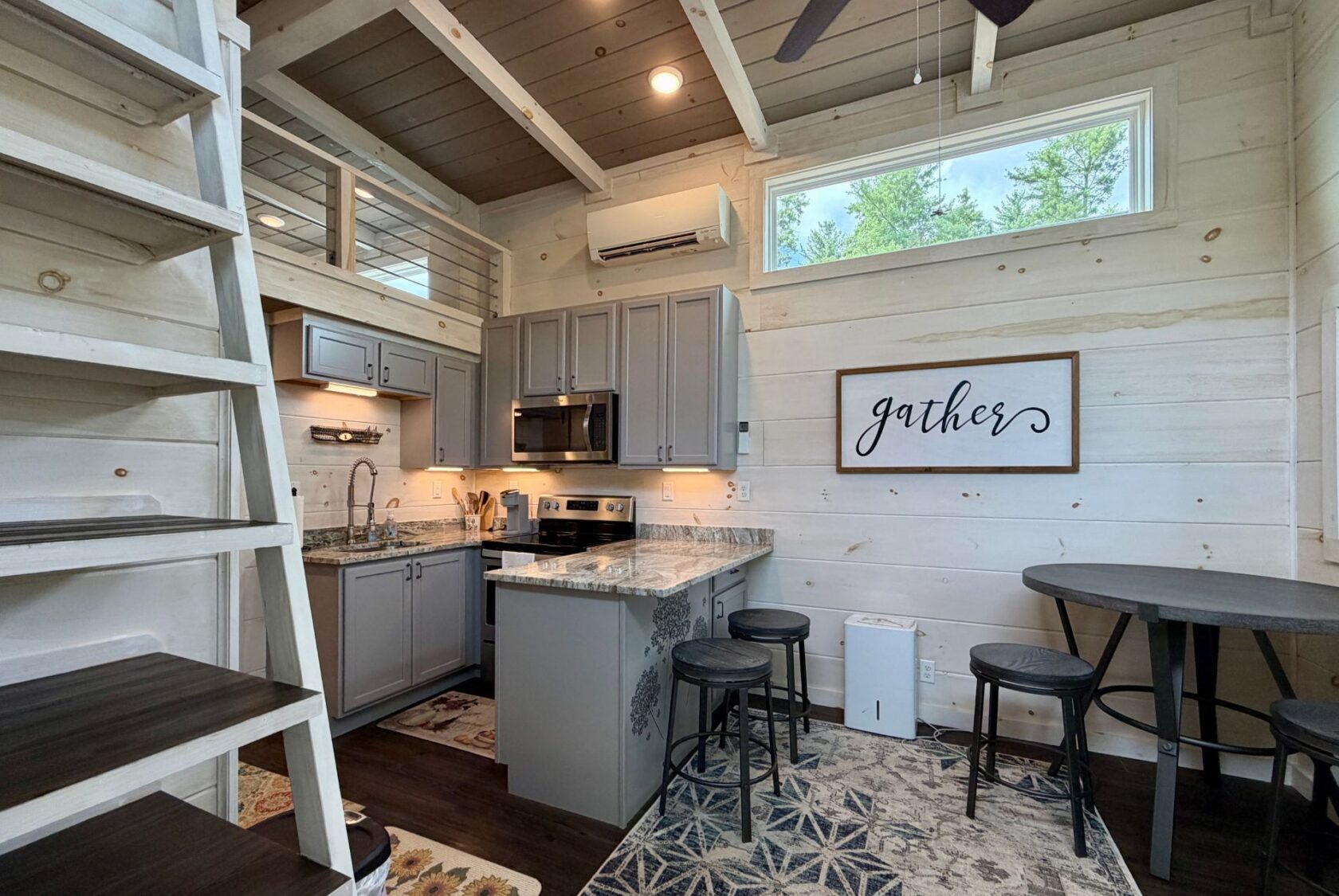 Modern Highland Hill Lane tiny kitchen with gray cabinets, marble island, “gather” sign, and loft ladder on the left.
