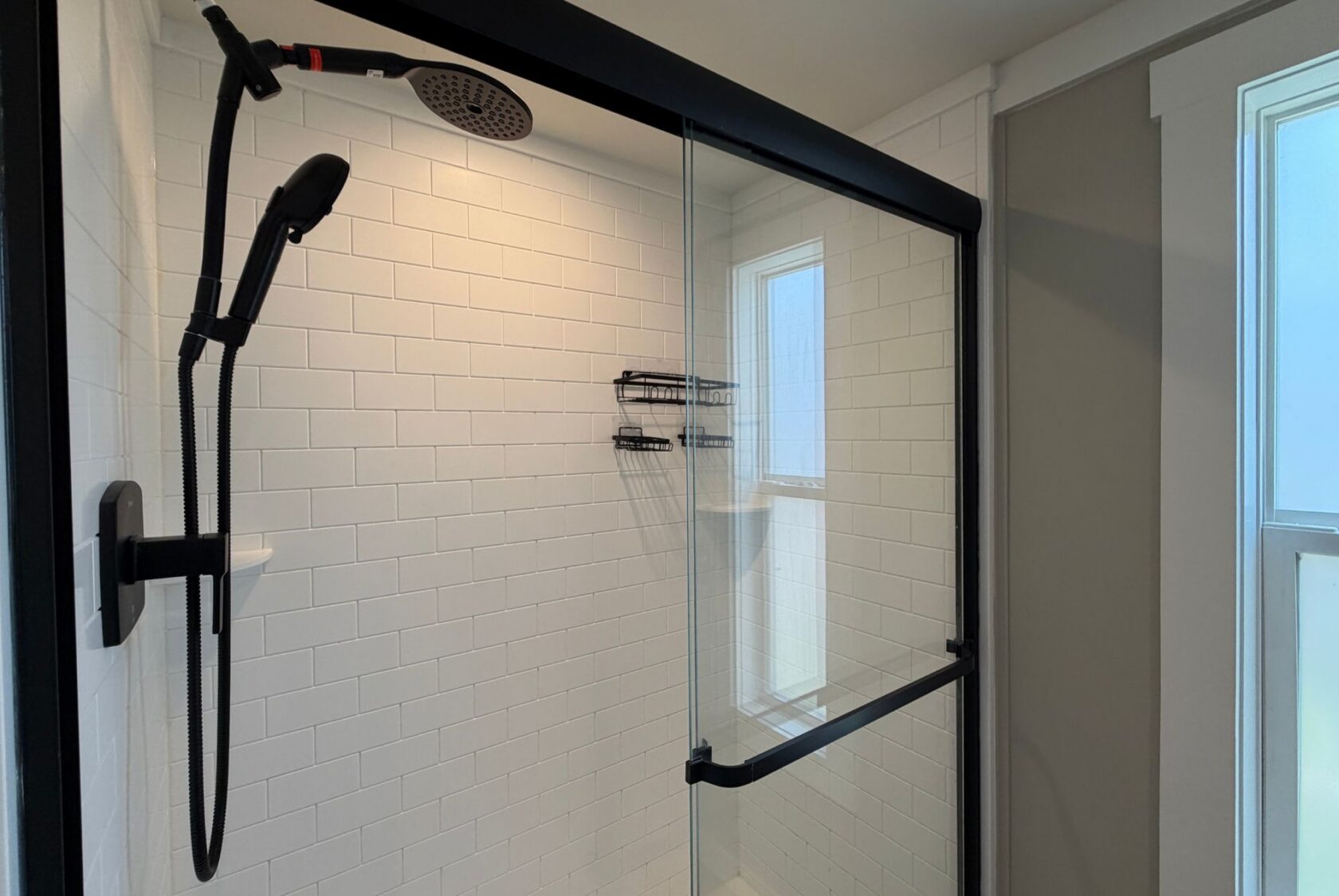 Modern shower at 103 Meandering Lane with white subway tiles, glass door, black fixtures, and natural light window.