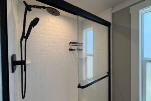 Modern shower at 103 Meandering Lane with white subway tiles, glass door, black fixtures, and natural light window.