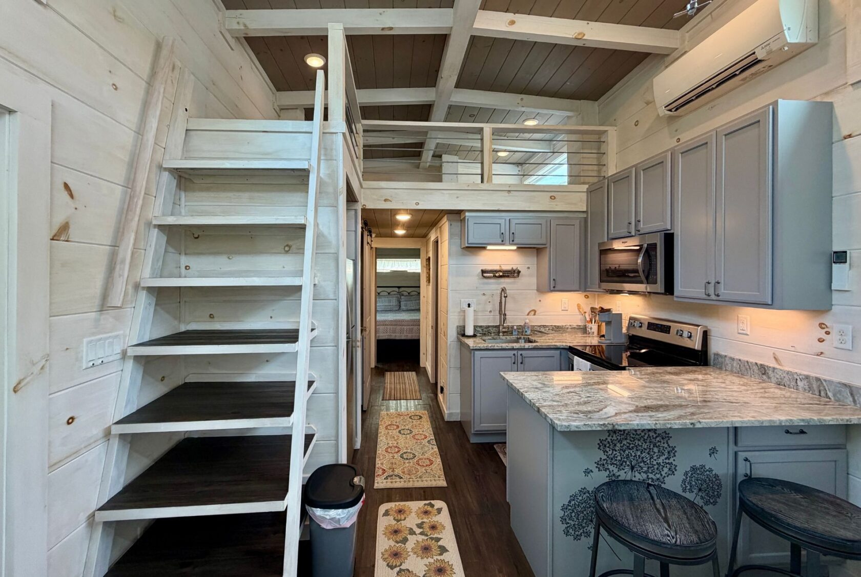 Tiny house interior on Highland Hill Lane with a loft, wooden stairs, modern kitchen, and gray cabinets.