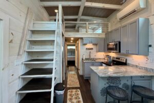 Tiny house interior on Highland Hill Lane with a loft, wooden stairs, modern kitchen, and gray cabinets.