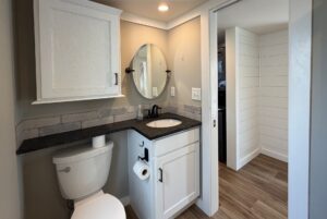 Small bathroom at 103 Meandering Lane with white cabinets, black countertop, round mirror, and adjacent laundry area.