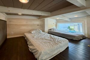 Two low beds with patterned bedding in a cozy Highland Hill Lane loft, featuring wood walls and a large window.