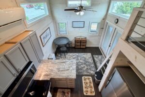 Discover 23 Highland Hill Lane: a tiny house featuring a kitchen, dining table, loft, stairs, and sunlit large windows.