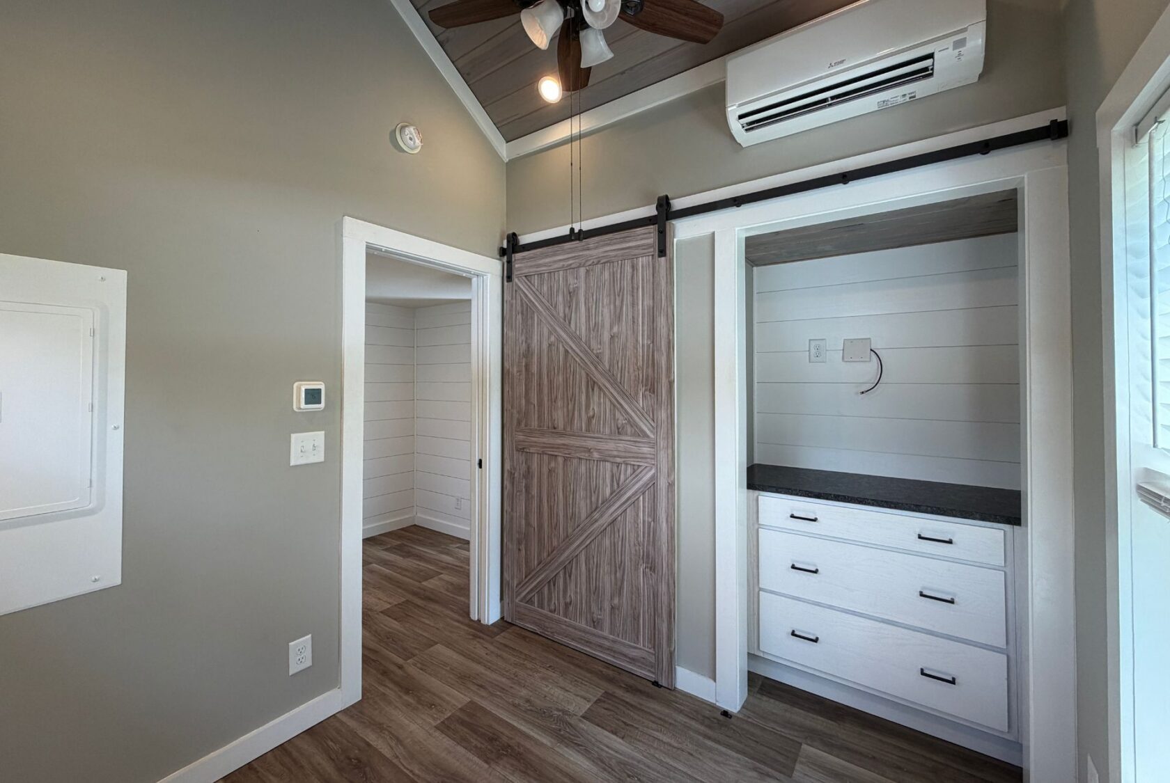 Small room on Meandering Lane with wood floors, gray walls, barn sliding door, built-in drawers, and ceiling fan.