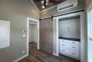 Small room on Meandering Lane with wood floors, gray walls, barn sliding door, built-in drawers, and ceiling fan.