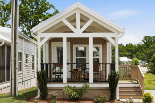 Charming small beige house with white trim on Mount Meadow Lane, featuring a porch, two chairs, and landscaped plants.
