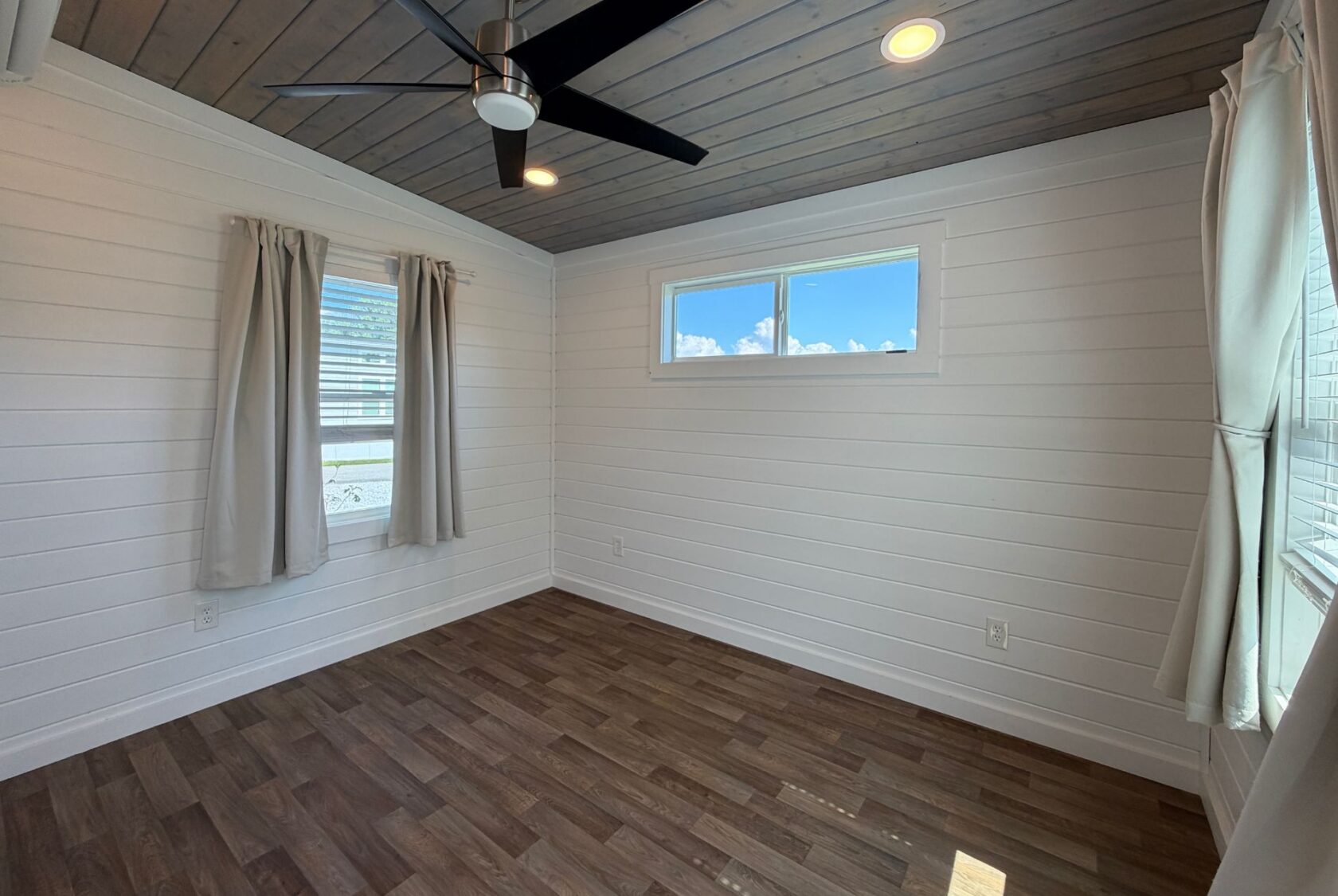 Charming small room at 103 Meandering Lane with wood floors, shiplap walls, large windows, and ceiling fan lighting.