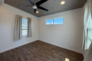 Charming small room at 103 Meandering Lane with wood floors, shiplap walls, large windows, and ceiling fan lighting.