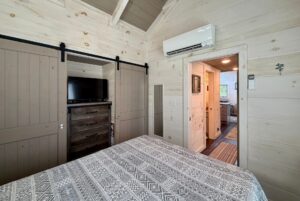 Cozy bedroom with wood walls, patterned bedspread, TV on dresser, and a view into the hallway at 23 Highland Hill Lane.