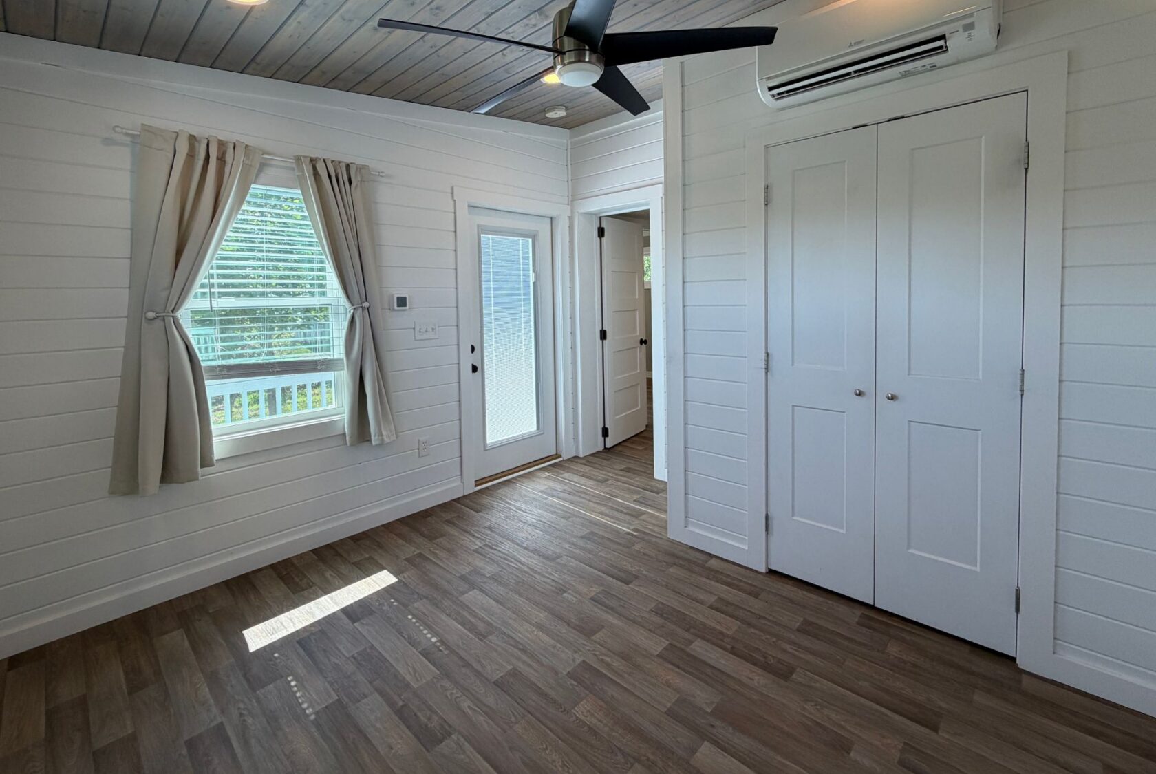 Bright room at 103 Meandering Lane with wood floors, white walls, ceiling fan, window, closets, and door outside.