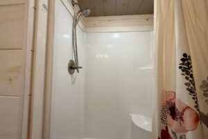 White shower with a silver showerhead, wooden trim, and a floral curtain—classic charm on Highland Hill Lane.