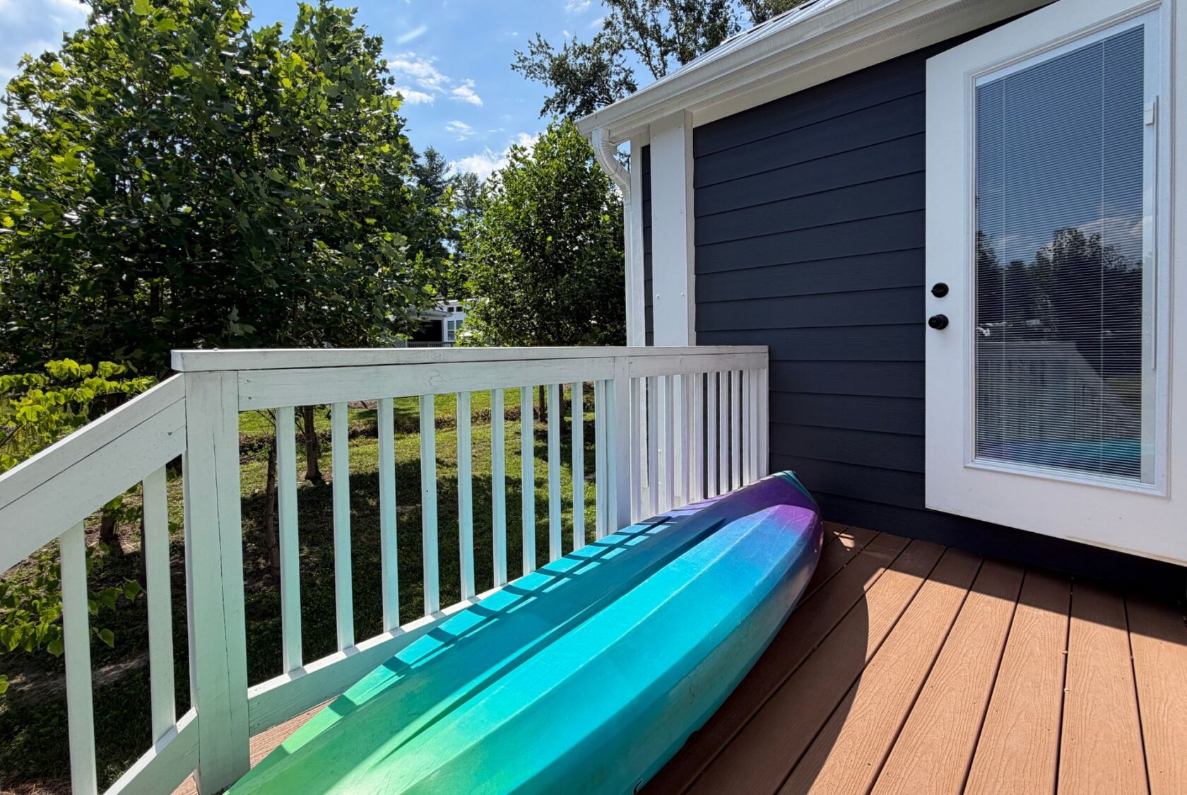 A blue and purple kayak rests on the deck at 103 Meandering Lane, beside white railings and a glass door.