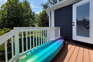 A blue and purple kayak rests on the deck at 103 Meandering Lane, beside white railings and a glass door.