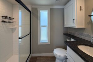 Modern bathroom at 103 Meandering Lane features glass shower, window, toilet, and dark countertop with white cabinets.