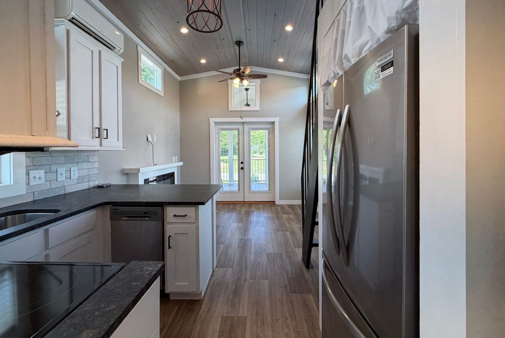 Modern kitchen at 103 Meandering Lane with white cabinets, wood floor, and French doors leading to a sunny outdoor space.