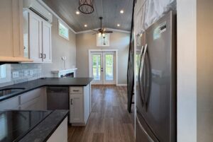 Modern kitchen at 103 Meandering Lane with white cabinets, wood floor, and French doors leading to a sunny outdoor space.