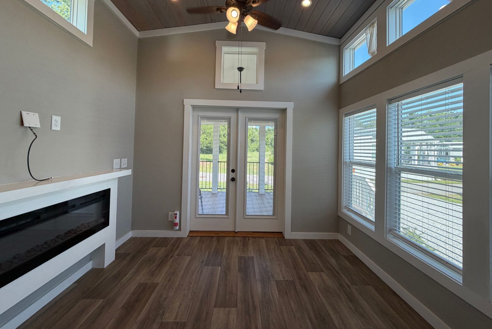 A small, bright room at 103 Meandering Lane with wood floors, large windows, a ceiling fan, and double glass doors outside.