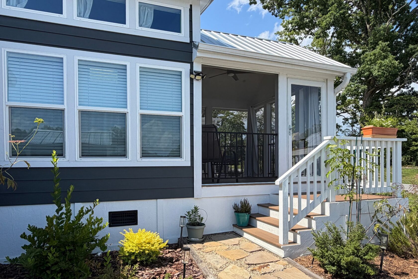 A house at 103 Meandering Lane with blue siding, white trim, potted plants, and stairs to a screened porch.
