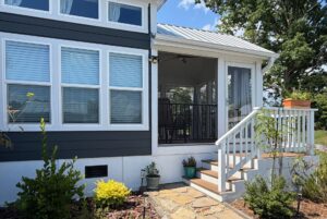 A house at 103 Meandering Lane with blue siding, white trim, potted plants, and stairs to a screened porch.