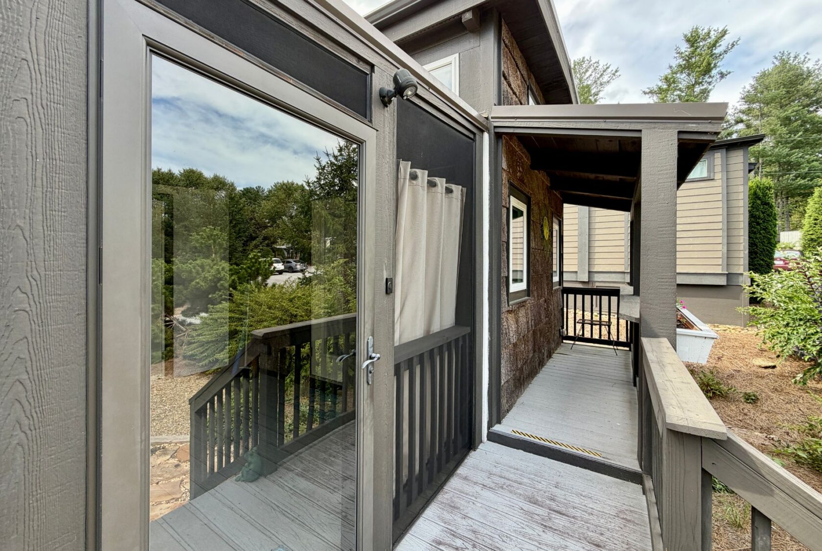 Glass door opens to a covered porch with wooden railings on Highland Hill Lane, surrounded by trees and greenery.