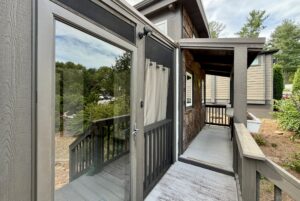 Glass door opens to a covered porch with wooden railings on Highland Hill Lane, surrounded by trees and greenery.
