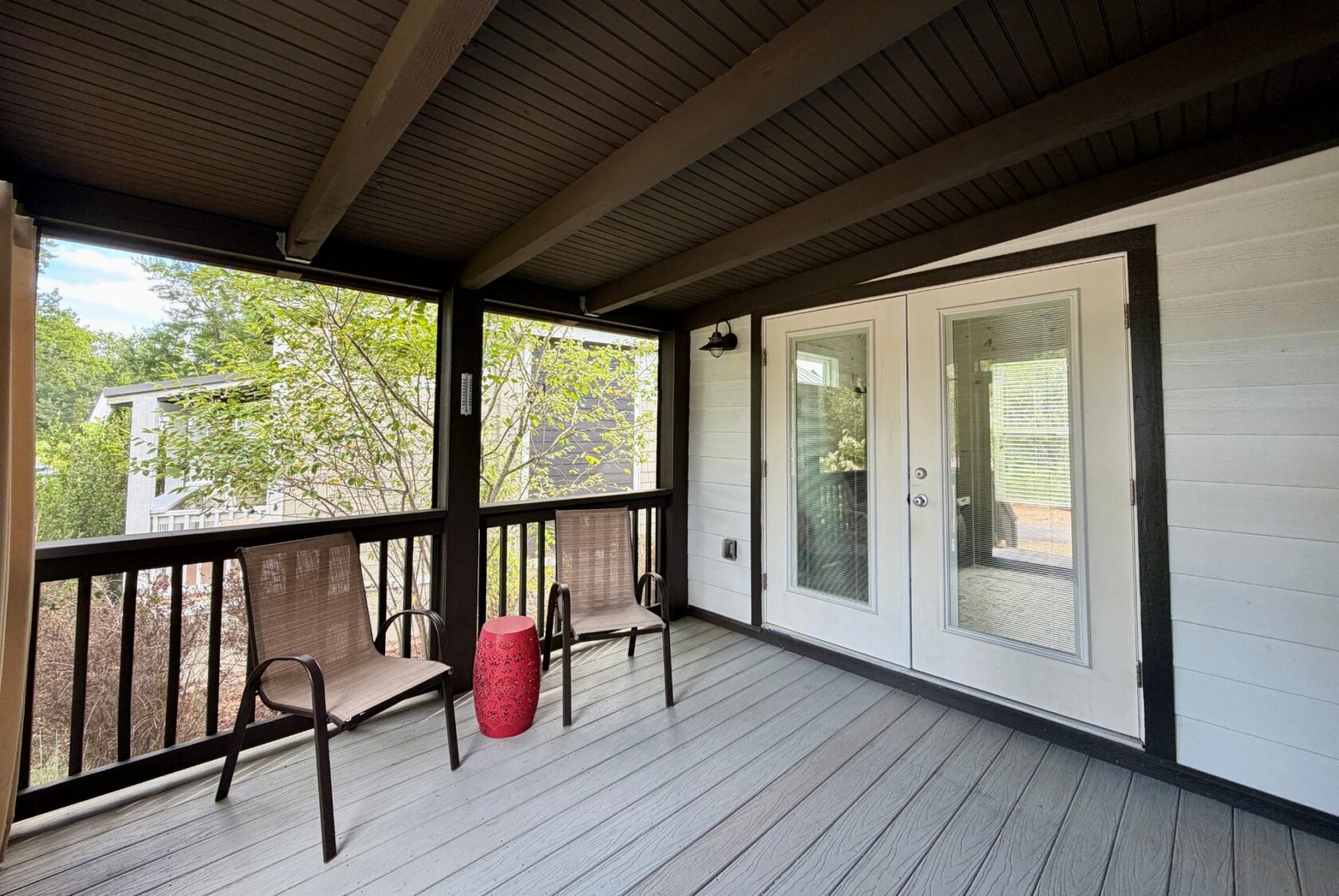 Covered porch on Highland Hill Lane with two chairs, red table, double glass doors; trees outside.