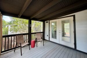 Covered porch on Highland Hill Lane with two chairs, red table, double glass doors; trees outside.