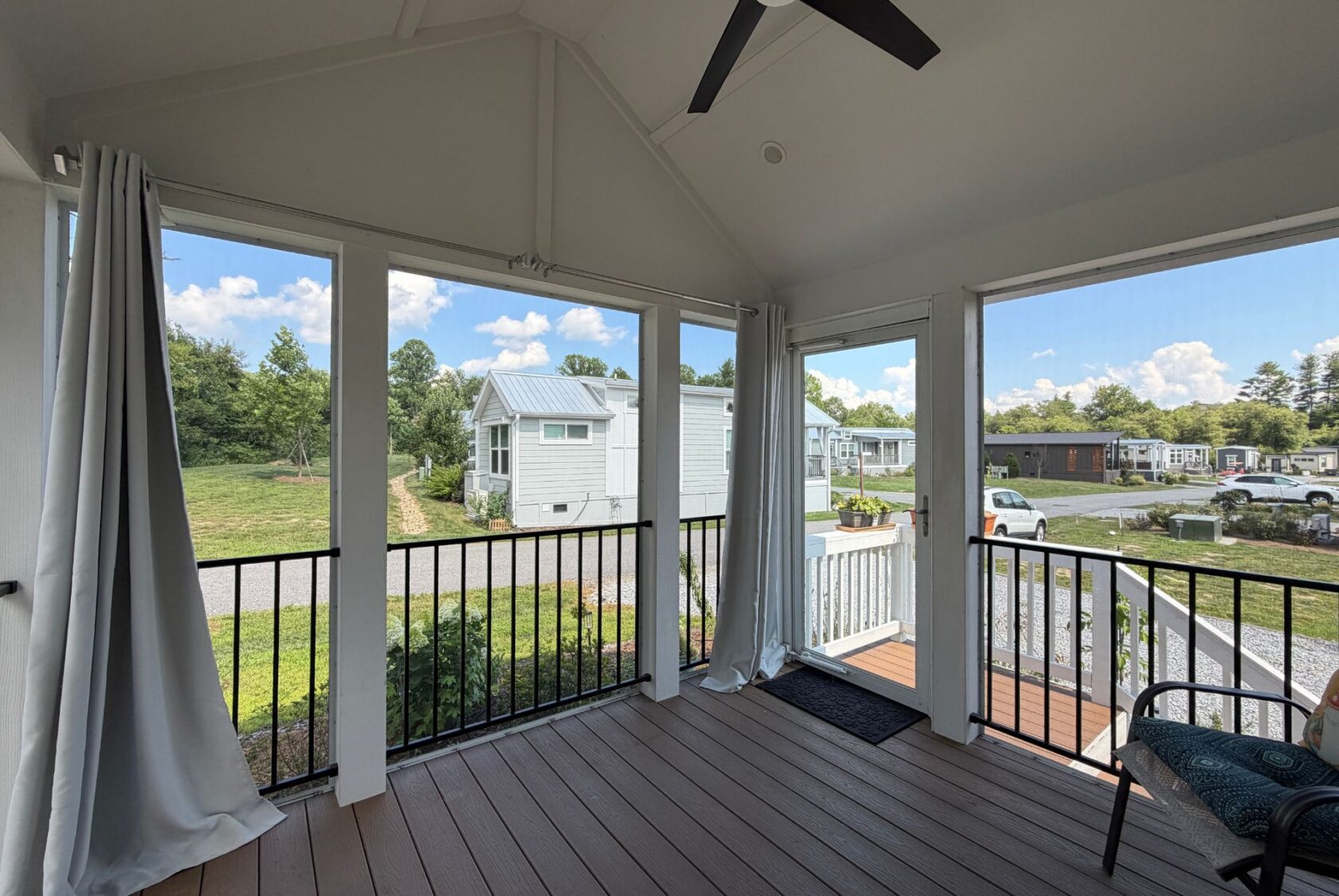 Screened porch with white curtains at 103 Meandering Lane, overlooking tiny homes and grassy areas under a blue sky.