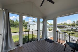 Screened porch with white curtains at 103 Meandering Lane, overlooking tiny homes and grassy areas under a blue sky.