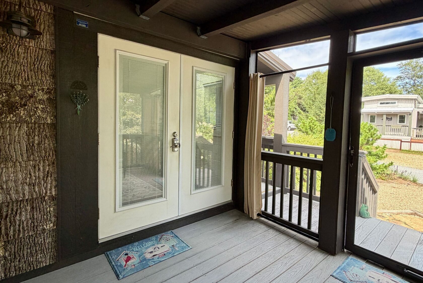 Screened porch on Highland Hill Lane features double glass doors, floor mats, and steps to a gravel pathway and greenery.