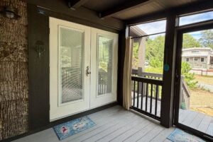 Screened porch on Highland Hill Lane features double glass doors, floor mats, and steps to a gravel pathway and greenery.