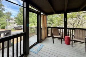 Screened porch on Highland Hill Lane: two chairs, red table, welcome mat, overlooks trees and a parked car on the street.