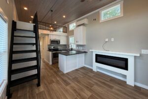 Modern tiny house interior at 103 Meandering Lane with loft, black stairs, kitchenette, fireplace, and wood floors.