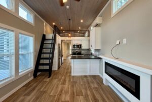 Modern tiny house interior at 103 Meandering Lane features wood floors, loft, kitchen, stairs, and electric fireplace.