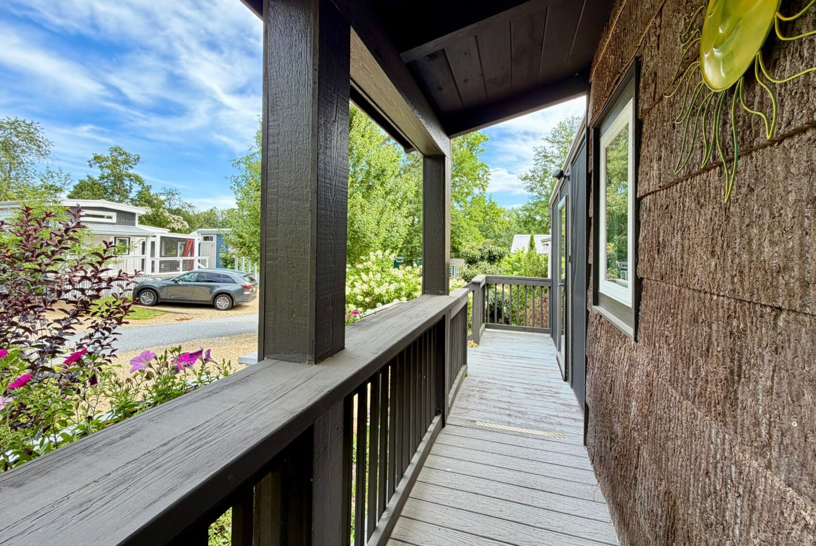 A wooden porch with railing overlooks Highland Hill Lane, a quiet street lined with cars, greenery, and tiny homes.