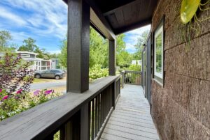 A wooden porch with railing overlooks Highland Hill Lane, a quiet street lined with cars, greenery, and tiny homes.