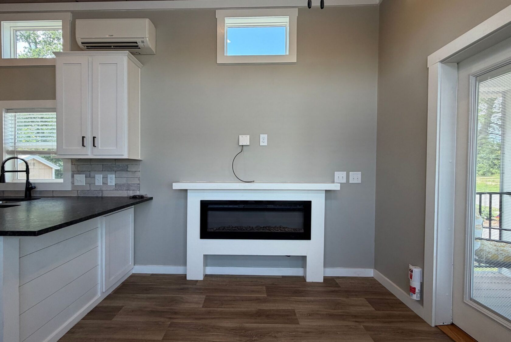 A wall-mounted electric fireplace at 103 Meandering Lane sits below outlets, beside the kitchen counter on wood floors.