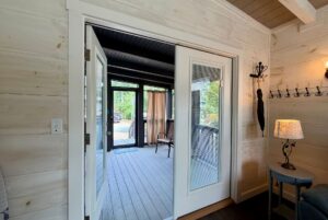 Open French doors on Highland Hill Lane connect a cozy, well-lit room to a screened-in porch with green views.