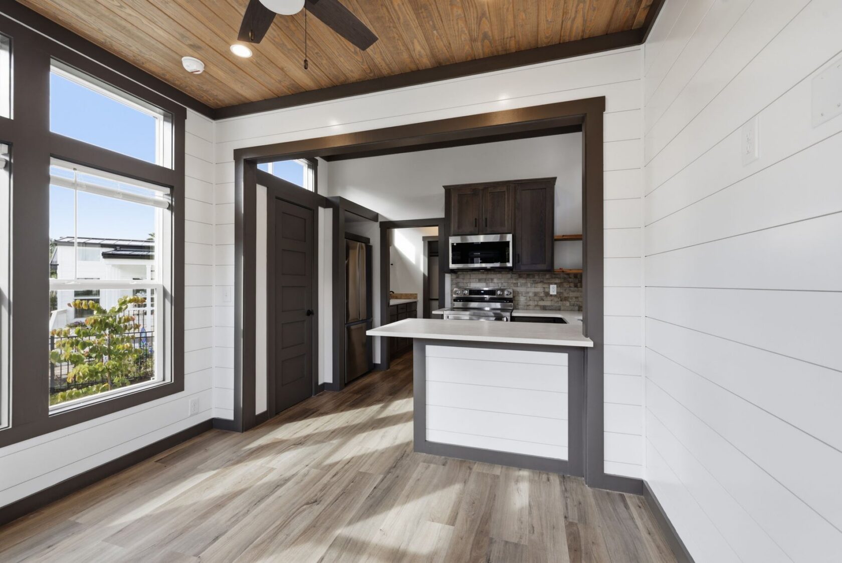 Modern kitchen with stainless steel appliances, wood floors, white shiplap walls, and large bright windows.