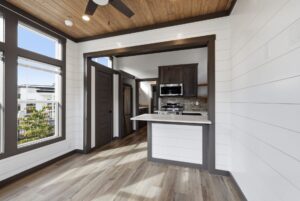 Modern kitchen with stainless steel appliances, wood floors, white shiplap walls, and large bright windows.