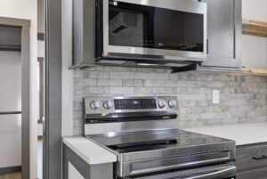 Modern kitchen with a stainless steel stove and microwave, gray cabinets, and a light tile backsplash.