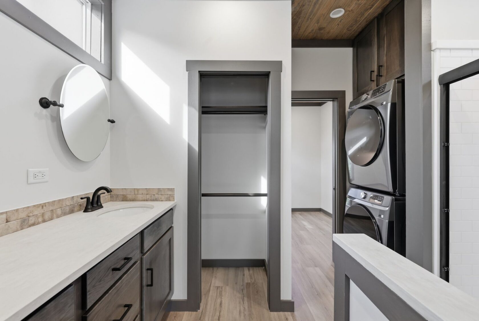 Modern bathroom with a vanity, circular mirror, empty closet, and stacked washer and dryer in the corner.