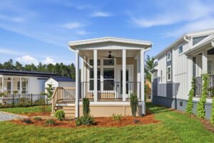 Small white house with front porch, steps, railing, and landscaped yard on a sunny day.