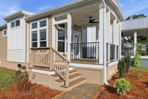 Beige house with white trim, a porch with black railing, steps, mulch, and a stone walkway in front.