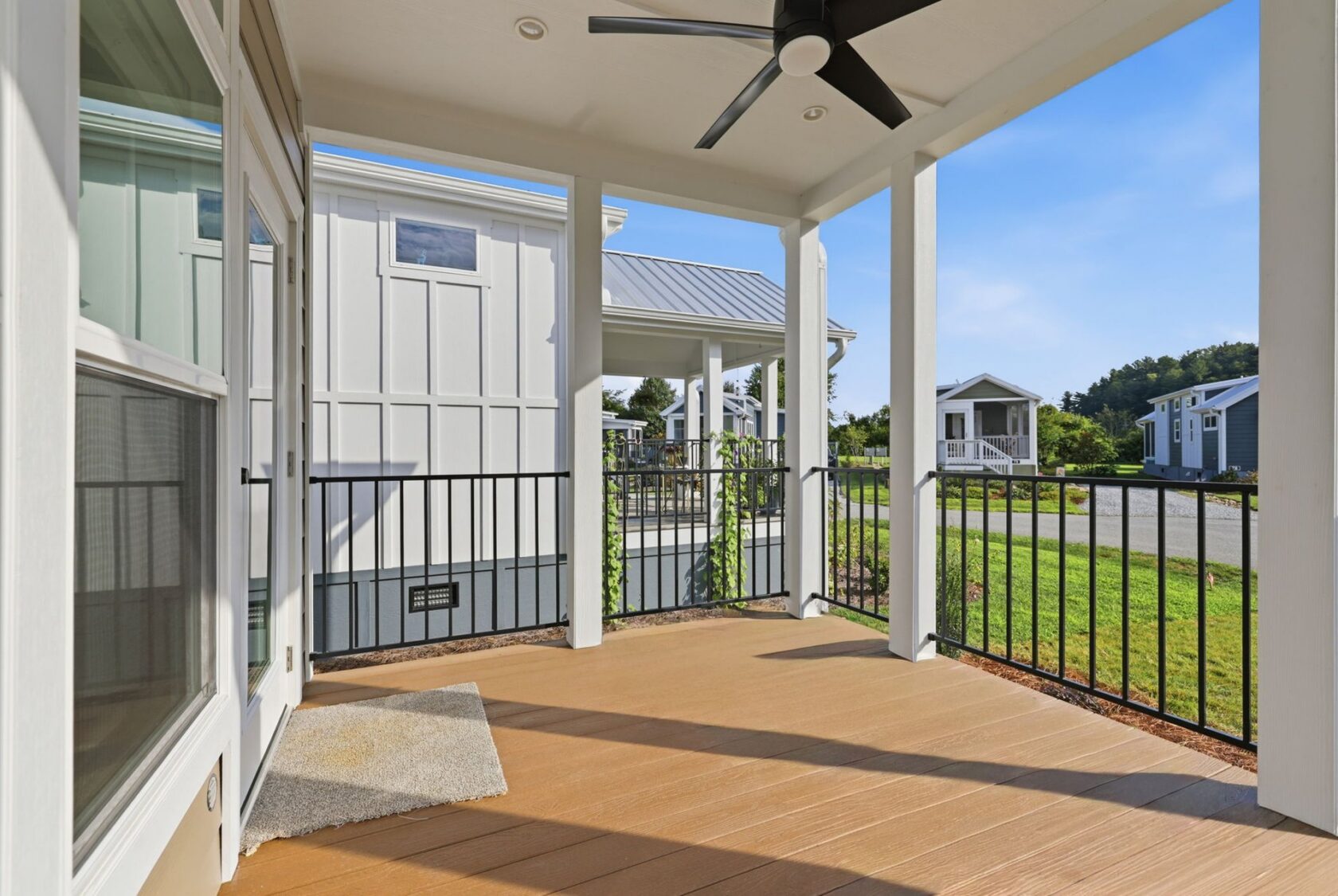 Covered porch with wood flooring and black railing, overlooking neighboring modern white houses and green lawn.