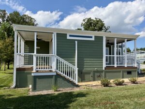 Charming green tiny house with white trim at 100 Meandering Lane, nestled on a grassy lawn under a partly cloudy sky.