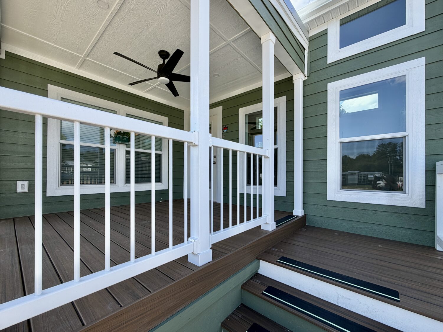 Green house exterior with white trim on Meandering Lane, wooden porch, black ceiling fan, and steps to the entrance.